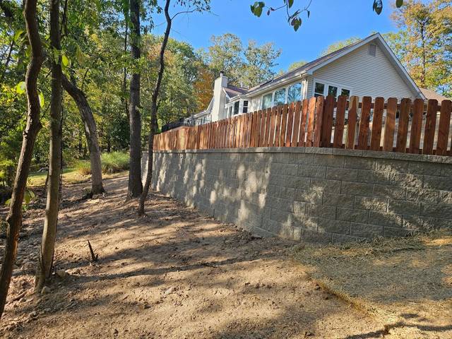 Tall block wall under a wood fence at the tree line